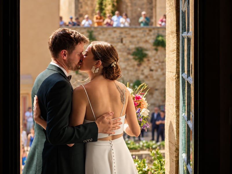 Un couple s’embrasse à son mariage, sous le regard des invités.